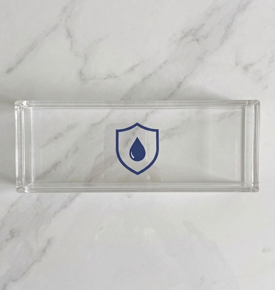 Child Safety Shield: a clear acrylic guard with a navy shield-and-droplet mark, photographed on a marble counter